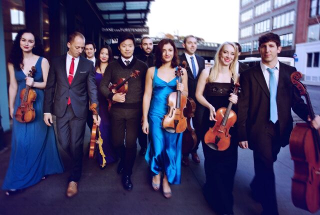 Ten musicians photographed walking while holding their string instruments.